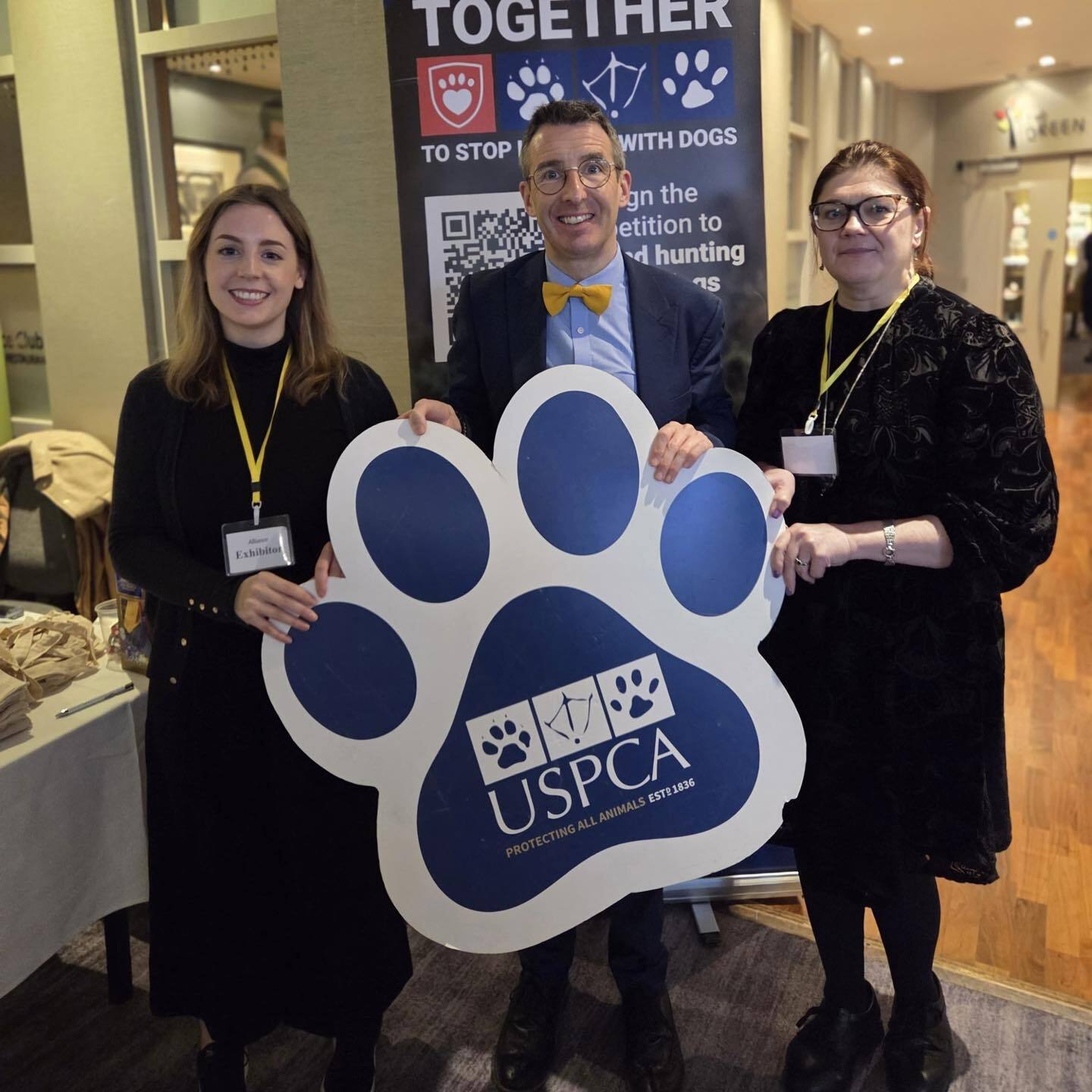 Two women and a man holding a paw print sign